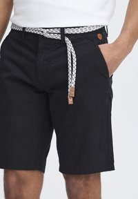 Shorts noirs en coton avec une ceinture texturée à motifs blancs et noirs. Comprend des poches latérales et un détail de logo marron.