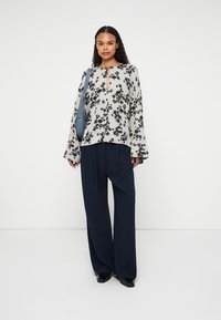 Bluzka w kwiatowy wzór, w jasnym beżu, z wycięciem w kształcie łezki, z długimi rękawami, zestawiona z granatowymi spodniami typu wide-leg i niebieską torebką na ramię.