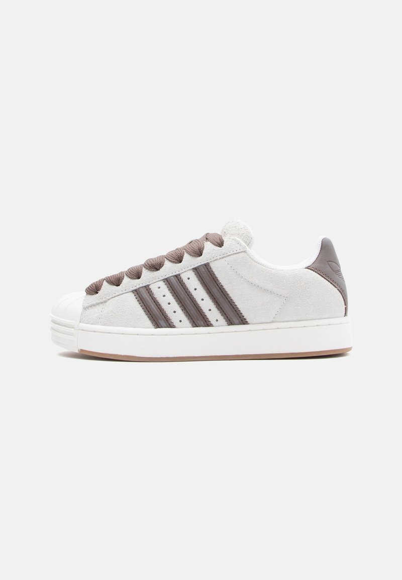 White suede sneakers with brown accents, featuring three dark stripes, a rubber sole, and a classic toe cap design.