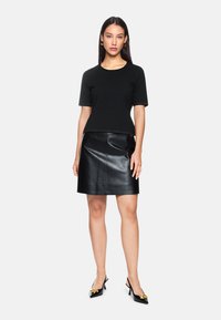 Schwarzes T-Shirt mit kurzen Ärmeln und Rundhalsausschnitt, kombiniert mit einem schwarzen Leder-A-Linienrock. Außerdem gehören spitze schwarze Absätze mit goldenen Akzenten dazu.