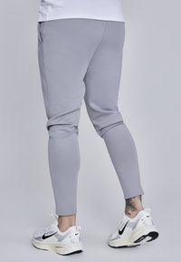 Grå atletiske joggingbukser med en tapered design, lavet af glat stof. Sammen med hvide sneakers med sorte accenter.