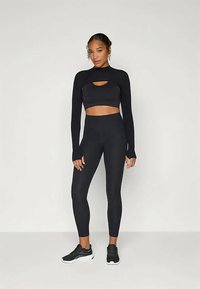 Conjunto de ropa deportiva negra que incluye una parte superior larga y corta con detalles recortados y leggings de tiro alto. Tejido suave y elástico con un diseño ajustado.