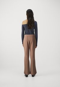 Námornícky off-shoulder top doplnený o vysoké hnedé nohavice so širokými nohavičkami. Hladká textura a priliehavý strih zvýrazňujú celkovú siluetu.