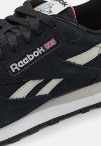 Näruppfattning av en svart Reebok Classic sneaker med vit logotyp, unionjackflagga, mocka-textur och vit och svart sula.