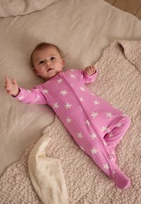 Body pour bébé rose à imprimé étoiles blanches, fabriqué en tissu texturé, avec une fermeture éclair à l'avant et des manches longues, posé sur une couverture douce de couleur neutre.