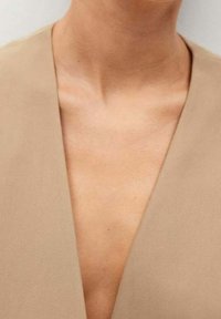 Beige V-Ausschnitt-Bekleidung mit glatter Textur, einem tiefen Ausschnitt und einem klaren, minimalistischen Design, das die darunter liegenden Hauttöne betont.