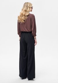Brązowa satynowa bluzka z bufkami w rękawach, zestawiona z czarnymi, szerokimi spodniami; gładkie tekstury i luźny krój z elastycznym pasem.