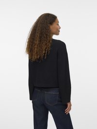 Zwarte, getexteerde trui met een cropped ontwerp en brede mouwen, gecombineerd met donkere spijkerbroek. Gezicht vanuit de achterkant, waarin de casual stijl wordt benadrukt.