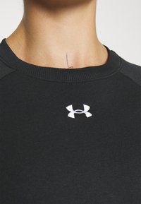 Sudadera negra con cuello redondo y textura acanalada. Presenta un logo blanco de Under Armour en el pecho.