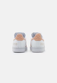 Vita sneakers med rosa accenter, grå hälen, textilmaterial och spräckliga sulor. Har tryckt text på utsidan.