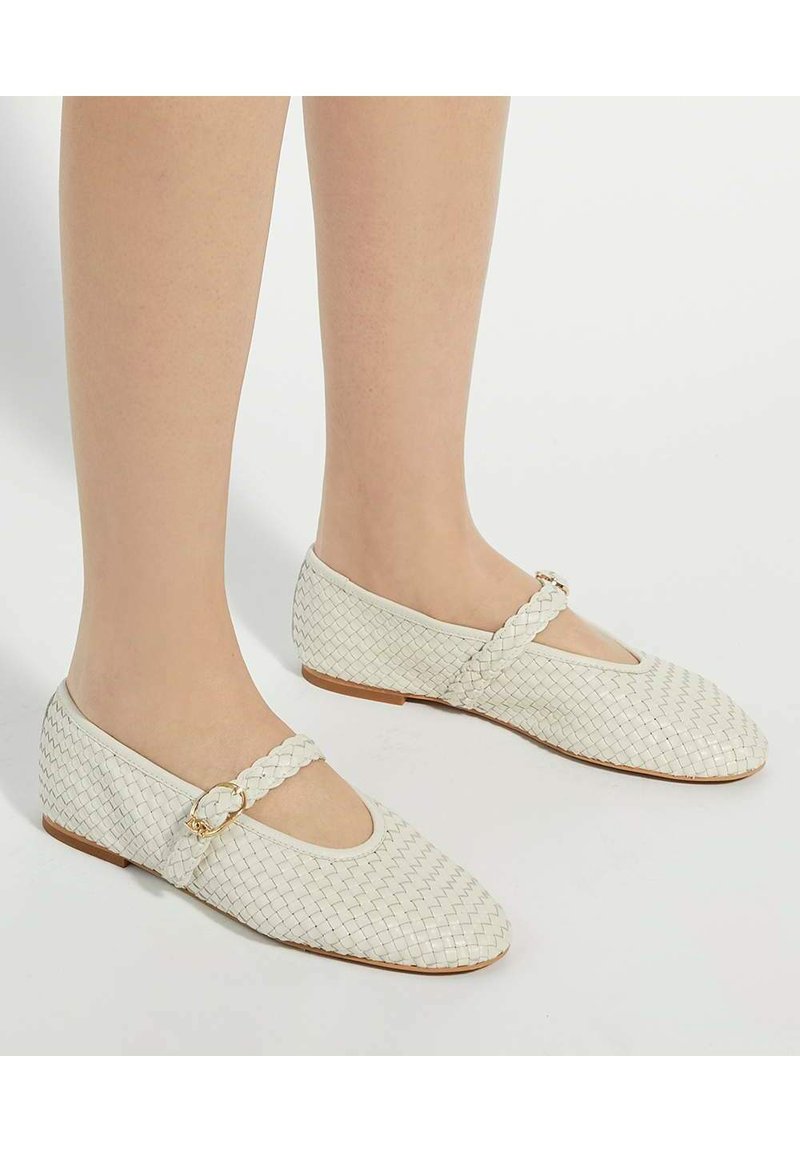 Witte geweven ballerina's met een gebogen teen, subtiele gouden hardware op een gevlochten band, en een platte bruine zool.