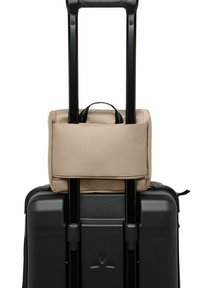 Zaino in tessuto beige sopra una valigia nera rigida, fissato dal manico telescopico. Texture liscia con dettagli in zip e un piccolo manico per il trasporto.