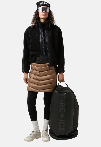 Black fleece jacket, padded brown chevron skirt, black leggings, beige sneakers, reflective sunglasses, black duffel bag with logo.