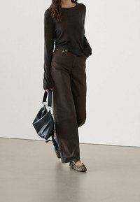 Brun långärmad skjorta och vida bruna jeans, kombinerat med leopardmönstrade ballerinaskor och bärande en svart väska med ett vitt band.