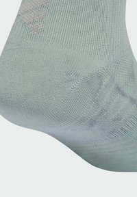 Svetlozelená ponožka vyrobená z textúrovanej látky. Má rebrovaný dizajn a jemný vzor v blízkosti oblasti prstov.