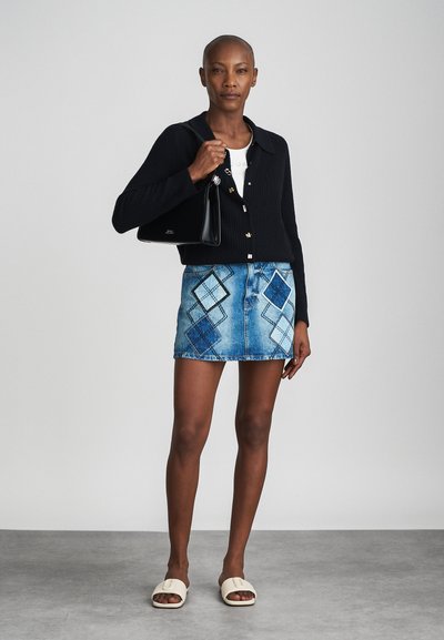 Cardigan nero in maglia, top bianco, gonna di denim con motivo a diamante blu e nero, borsa nera e sandali scivolati beige.