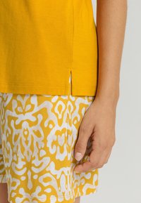 Geel kortmouwenshirt met zijslitsen, gecombineerd met gestreepte shorts in geel en wit, met een draaiend abstract ontwerp.