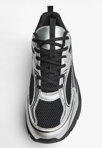 Crne mrežaste tenisice sa srebrnim sintetičkim detaljima. Imaju crne vezice, podstavljeni jezik i strukturiranu gumenu potpeticu.