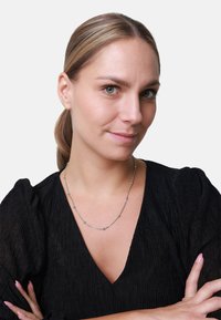 Silberne Halskette mit kleinen runden und ovalen Akzenten, getragen zu einem schwarzen strukturierten Oberteil mit Puffärmeln und V-Ausschnitt.