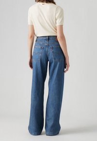 Siniset leveälahkeiset farkut korkealla vyötäröllä, joissa on takataskut ja kontrastivärinen ommel. Yhdistetty kevyenväriseen kapeaan paitaan.