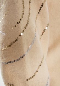 Maglione a maglia di un beige chiaro con una finitura testurizzata, impreziosito da paillettes metalliche in oro, argento e tonalità iridescenti disposte in motivi curvi.