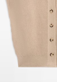 Beige stickat tyg med vertikal ribbad struktur och en rad med fyra bruna knappar längs höger sida på vit bakgrund.
