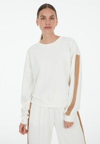 White sweatshirt with long sleeves, featuring a brown stripe along the sleeves. Smooth texture, round neckline, relaxed fit at the hem.
