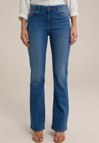 Siniset farkkulegginsit, joissa on korkea vyötärö, etutaskut, hieno haalistuminen ja napitus. Yhdistetty vaaleanruskeisiin sandaaleihin.