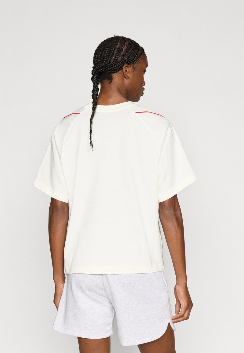 Valge lühikeste varrukatega t-särk, mis on õlgadel punaste aktsentidega ja valmistatud pehmest kangast. Särgil on lõdva istuvuse ja kastikujuline vorm.