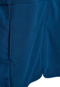 Niebieska polarowa kurtka z teksturowaną powierzchnią, posiadająca boczną kieszeń oraz gładkie wykończenie wzdłuż brzegów. Projekt jest prosty i funkcjonalny.