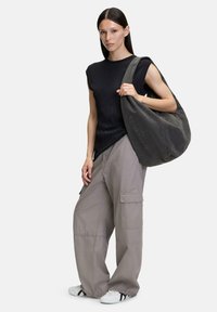 Szara torba hobo o miękkiej fakturze i detalach z logo, w połączeniu z czarnym prążkowanym topem i luźnymi szarymi spodniami cargo. Obuwie: białe z czarnymi akcentami.