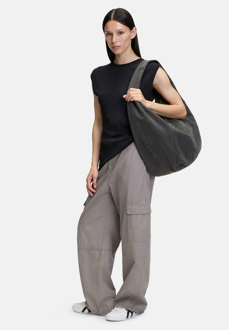 Szara torba hobo o miękkiej fakturze i detalach z logo, w połączeniu z czarnym prążkowanym topem i luźnymi szarymi spodniami cargo. Obuwie: białe z czarnymi akcentami.