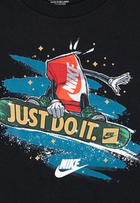 Juodas medvilnės marškinėliai su raudono gėrimo puodelio grafika ant riedlentės, su užrašu "TIESIOG DARYK TAI." ir Nike logotipais žaliomis ir auksinėmis akcentais.