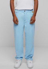 Light blue corduroy pants with a straight cut, featuring front pockets and a small embroidered logo on the waistband. Smooth texture.