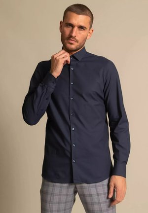Navy blue button-up shirt with a pointed collar and long sleeves, featuring a smooth texture and contrasting buttons.