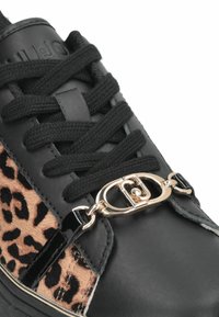 Baskets noires avec des panneaux à imprimé léopard, finition texturée, conception à lacets noire, et accents en or brillant sur le côté.