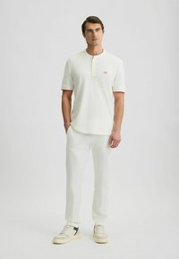 Polo alb cu maneci scurte și guler roșu, împreună cu pantaloni albi și adidași bej cu accente verzi. Textură netedă.