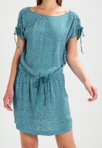 Turquoise katoenen jurk met witte stippen, korte mouwen, geplooide strikjes op de schouders en een taillekoord voor een verstelbare pasvorm.