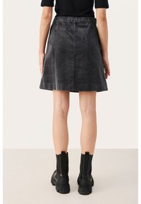 Jupe en velours côtelé noire avec une taille élastique, en forme de A, et une texture subtile. Portée avec des bottines noires à semelle épaisse.