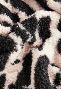 Gros plan d'un tissu doux et texturé avec un motif rayé irrégulier noir et beige et une surface bouclée et moelleuse.