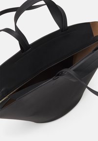 Sac cabas en cuir noir avec ouverture sur le dessus, doté de deux poignées solides et d'une fermeture éclair dorée sur un côté. Intérieur de couleur marron contrastante.