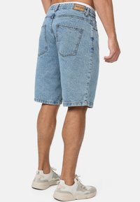 Shorts en denim bleu clair avec une coupe décontractée, cinq poches et une étiquette en cuir beige avec logo à la taille arrière. Ourlets cousus et distorsion minimale.