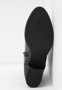 Semelle en cuir noir avec un motif de grip texturé. Présente une forme arrondie et un embout renforcé. Design minimaliste sans matériel visible.