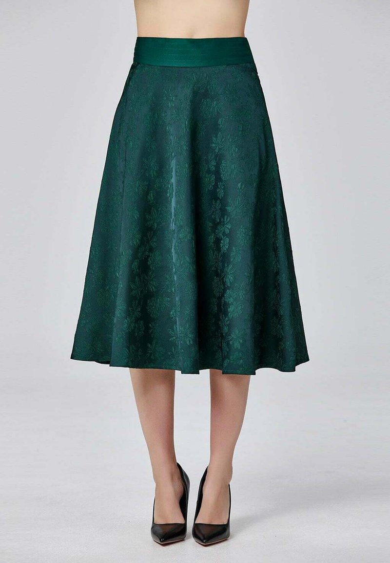 Jupe midi en satin vert avec motif floral, taille large, forme évasée, texture lisse, portée avec des escarpins noirs.