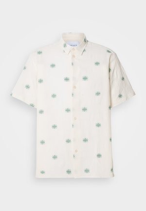 Chemise à manches courtes de couleur crème en lin, avec un motif brodé de fleurs teal et des boutons beiges sur le devant.