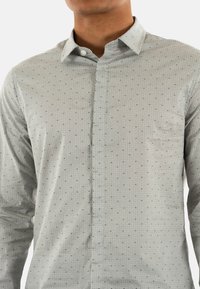 Chemise boutonée gris clair avec un motif textur é, dotée d'un col rabattu, de manches longues et d'une poche poitrine.