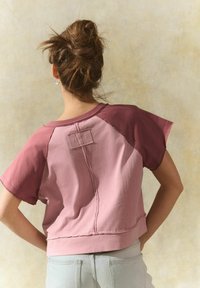 Korte mouwen, cropped t-shirt in twee tinten roze. Heeft een gestikte naaddetail en een patch op de rug. Zachte stof met een relaxte pasvorm.
