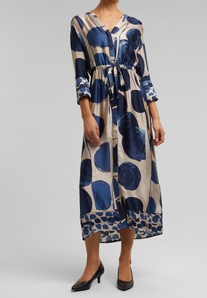 Langes, marineblaues und beigefarbenes gemustertes Kleid aus seidig glänzendem Material mit einem taillierten Gürtel, V-Ausschnitt und 3/4-Ärmeln im gepunkteten Design.