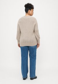 Beige strikket genser med et teksturert fiskebensmønster, rund hals og lange ermer, kombinert med blå rett ben-jeans.