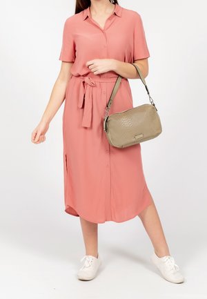 Kurzärmeliges, knöpfbares Kleid in sanftem Korallton, mit Taillengürtel und Seitenschlitzen. Handtasche in hellem Olivgrün, mit strukturierter Oberfläche, über der Schulter getragen.